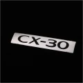 Srebrna blaszka z logiem CX-30 na oryginalnym dywaniku welurowym luxury do Mazdy CX-30.