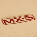 Haftowane logo MX-5 na beżowych dywanikach welurowych do Mazdy MX-5 NB.