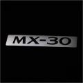 Metalowa blaszka z logiem MX-30 na dywaniku materiałowym do Mazdy MX-30.