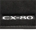 Białe logo Mazdy CX-80 na dywanikach welurowych.